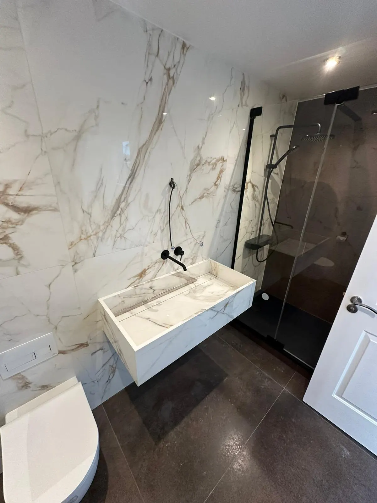 Bathroom renovation in London: marble-effect walls, dark floor and black shower fittings