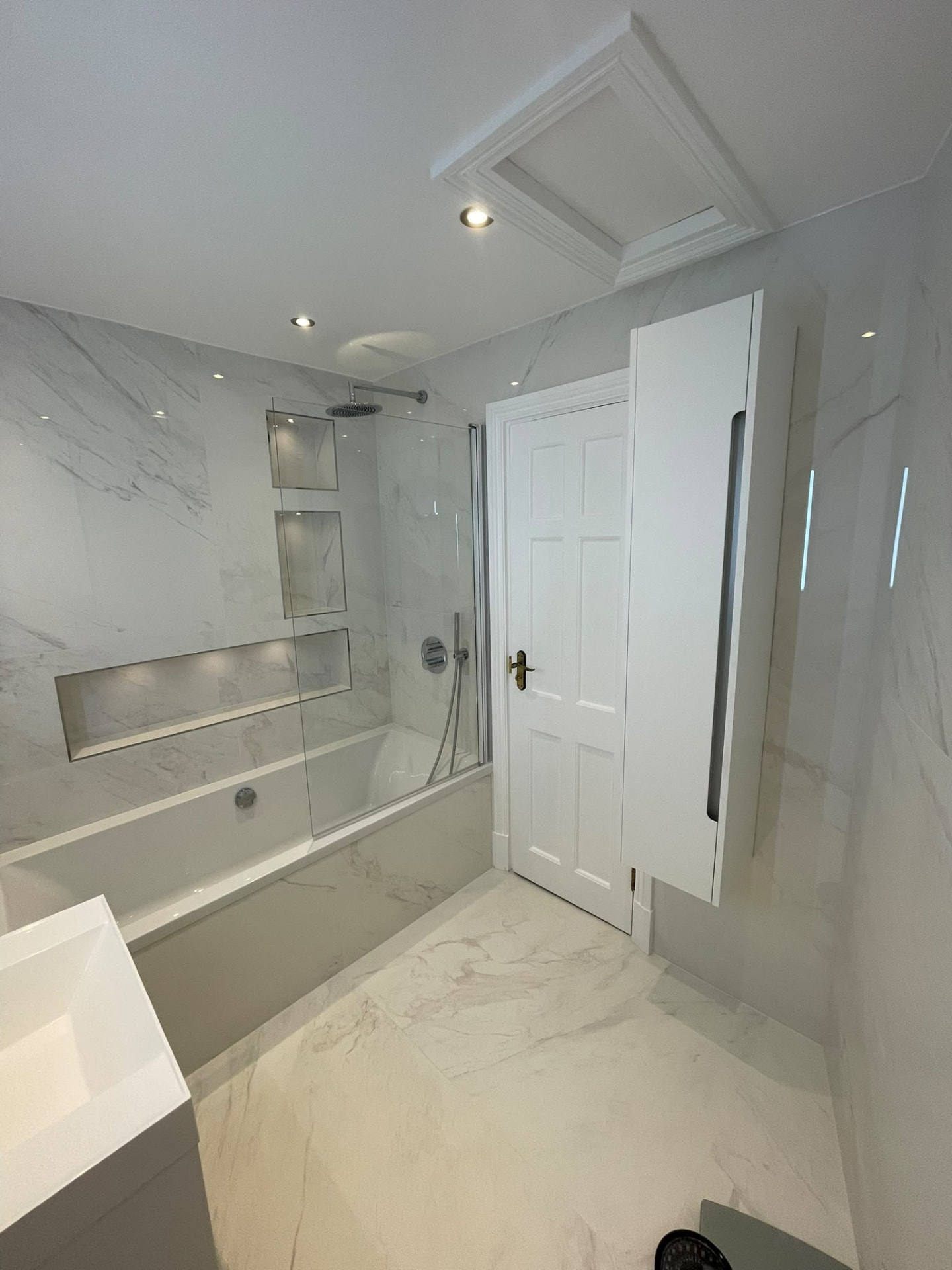 Bathroom renovation in London: pale marble-effect bath with shower screen and wall cabinet