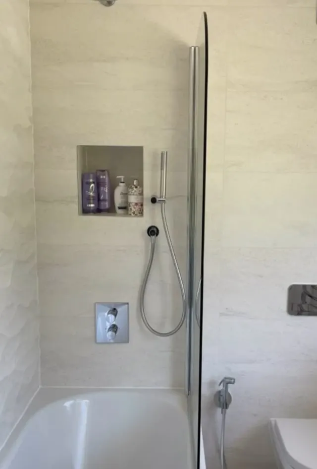Bathroom renovation in London: stone-effect bath and shower wall with tiled niche