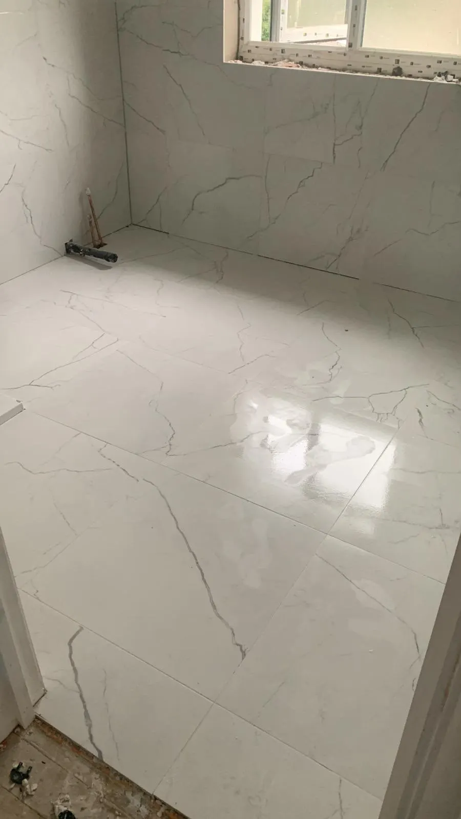 Bathroom renovation in London: large marble-effect wall and floor tiles being installed