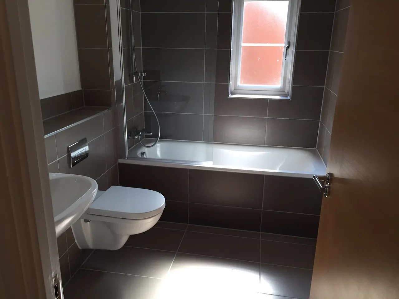 Bathroom renovation in London: compact bathroom with dark brown tiles, bath screen and wall-hung toilet