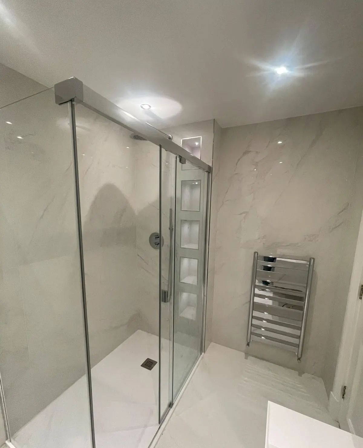 Bathroom renovation in London: marble-effect shower with niches and heated towel rail